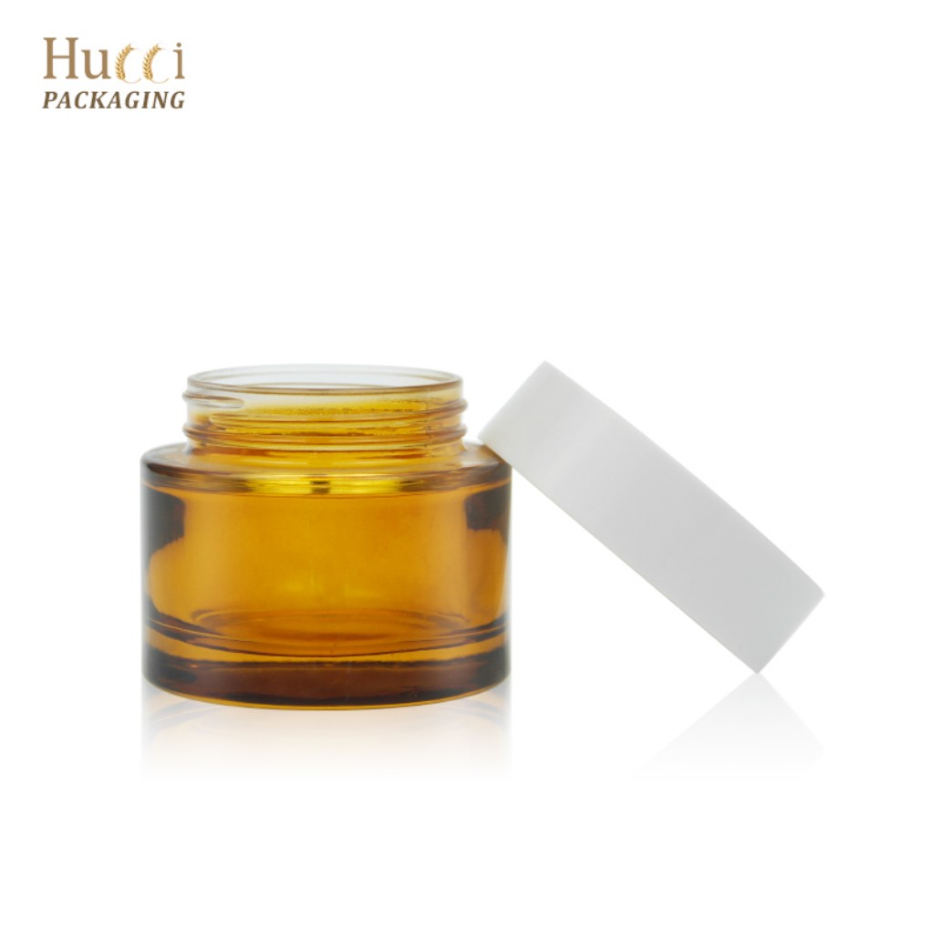 70g Opened Amber Glass Face Cream Jar with Leaning White PP Cap White Background}